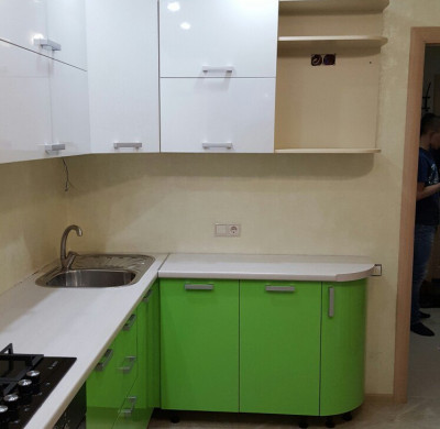 Зелёная угловая кухня с радиусными фасадом и белым верхом
